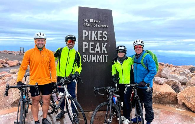 Four bikers take a photo together at the Pikes Peak Summit sign.